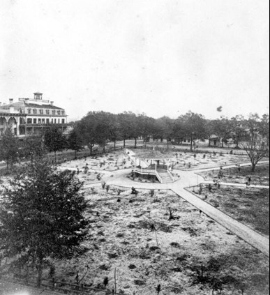 A small gazebo sits in the middle of a cleared park. Six straight walkways radiate out from the gazebo. A large hotel is visible at the left of the image.